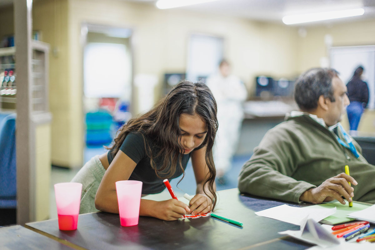 A young girl bends over a desk writing on a piece of paper